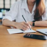 A woman sitting with a laptop and notepad working on determining goals