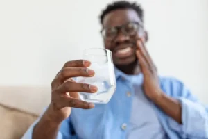 Smiling man with blue shirt and glasses holding a glass of water