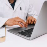 A doctor in a white coat typing on their laptop