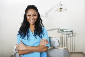 A woman smiling in dental scrubs by an exam chair